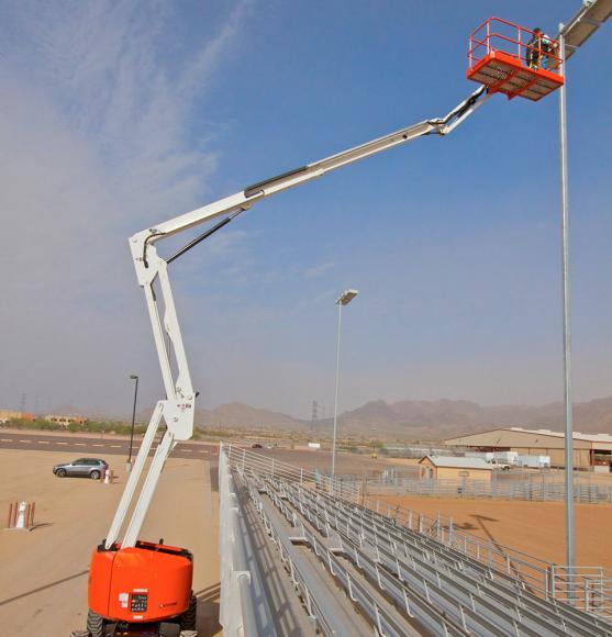 White and orange boom lift elevated reaching over stadium seating to repair light
